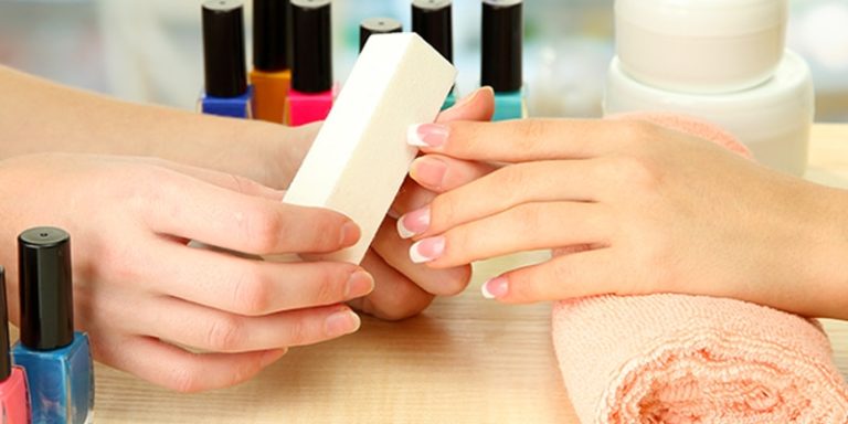 Nail technician filing a client's nails beside a row of polish bottles