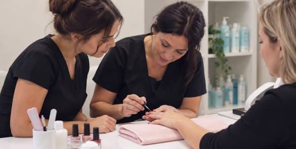Illustration of a tutor demonstrating a manicure while a learner watches in a beauty training room.