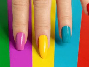 Shaped nails painted yellow, blue, green and red against a colourful background