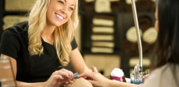 Smiling nail technician painting a client's nails in a salon