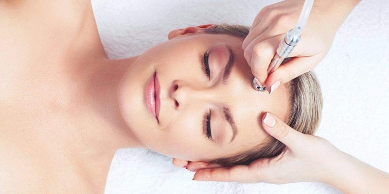 A therapist performing a microdermabrasion treatment on a client’s face with a handheld machine